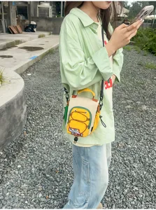 Une personne utilise son téléphone dehors et porte un sac bandoulière jaune et crème aux détails colorés