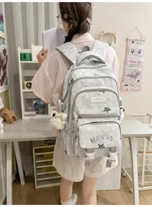 Vue arrière d’une personne portant un sac gris clair, avec plusieurs poches zippées et un ours en peluche.