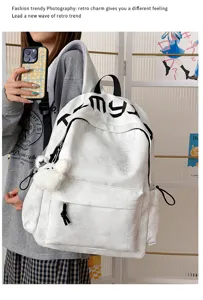 Gros plan sur un sac à dos blanc, avec étoiles en relief, lettrage noir et pompon pelucheux