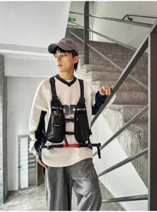 Black multi-pocket nylon chest bag worn over a sweatshirt, shown on a model beside a stairway