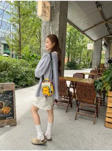Une femme porte dehors un petit sac jaune illustré, avec panneaux colorés et bandoulière réglable.