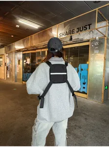 Rear view of a model wearing a black nylon chest pack with adjustable straps and reflective strip