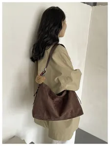Vue de côté d’un modèle portant un sac brun effet daim avec un petit pendentif ourson en peluche
