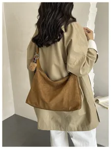 Vue de dos d’une personne portant un sac bandoulière souple en suédine brune avec un pompon doux