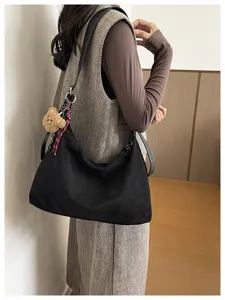 Vue de profil d’une personne portant un sac noir texturé avec un pendentif ourson et cordon bicolore