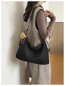 Détail d’un sac souple noir mat porté par un modèle, avec un ours en peluche et un ruban à carreaux