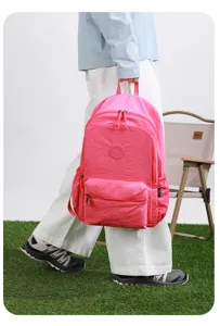Eine Person trägt einen rosa Nylonrucksack mit Reißverschlusstaschen neben einem Campingstuhl