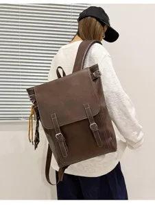 Rückansicht eines braunen Kunstlederrucksacks mit Klappe, Metallschnallen und gewebtem Anhänger