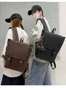Zwei Models tragen braune und schwarze Rucksäcke mit Klappe, Schnallenriemen und Entenanhängern.