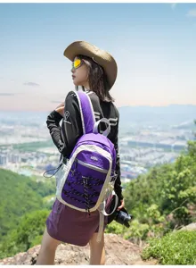 Wanderin mit violett-weißem Rucksack auf einem Bergpfad, Stadt und Hügel im Hintergrund