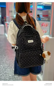 Vue arrière d’un sac noir à pois blancs porté avec un pendentif chien en peluche en centre commercial