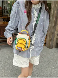 Une personne porte dehors un petit sac jaune et blanc à cordon, avec bord vert et sangle noire.