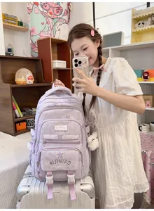 Sac à dos lilas à étoiles, avec poches zippées superposées et pompon, posé sur une valise