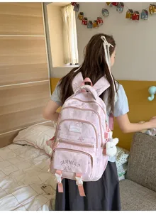 Vue de dos d’une élève portant un sac rose à compartiments et un petit lapin blanc en peluche