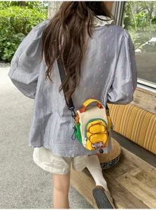 Vue arrière d’une personne portant un petit sac jaune, crème et vert avec poche zippée dehors