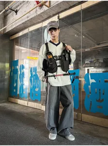 Streetwear model wearing a black utility chest rig over a white sweatshirt, with gray trousers