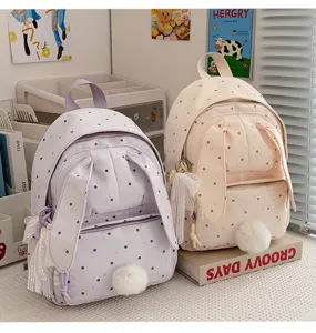 Deux sacs pastel à motifs de pois et cœurs, pompons doux et pampilles, posés sur des livres