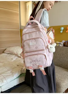 Une élève porte un sac à dos rose à plusieurs poches, avec broderie et breloque blanche en peluche