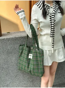 Lifestyle view of a green plaid tote with twin handles and a small white label, carried by a model