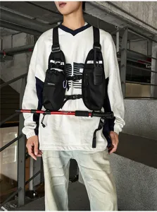 Black chest pack worn over a white sweatshirt, showing adjustable straps and front zip pockets