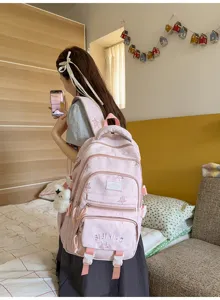 Vue de dos d’une personne portant un sac rose pâle à plusieurs compartiments avec un ours en peluche