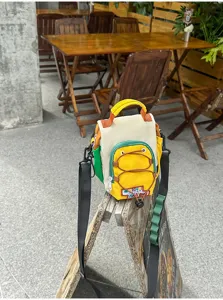 Petit sac multicolore avec poche zippée jaune et poignée, posé sur un support en bois dehors