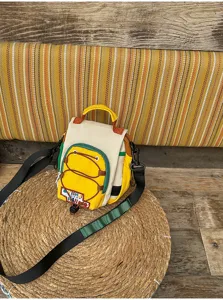Sac jaune et crème avec cordon devant, sangles noires et poignée, posé sur un tapis tressé