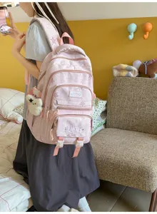 Vue de côté d’une élève portant un sac à dos rose avec poches zippées et un pendentif en peluche