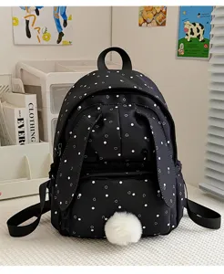 Gros plan sur un sac à dos noir à pois blancs, avec poche avant zippée et pompon blanc duveteux