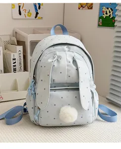 Sac à dos bleu clair à pois, avec longues oreilles de lapin et pompon doux, posé près d'un bureau