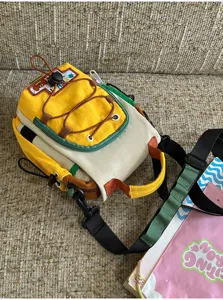 Vue d’un sac jaune et crème à empiècements verts, avec cordons bruns et bandoulières noires