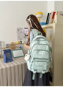 Vue portée d’un sac à dos vert menthe à plusieurs poches zippées, avec pompon blanc
