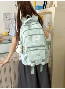 Vue de dos d’une élève avec un sac à dos vert pâle, des poches zippées et un pendentif en peluche