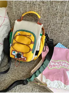 Vue de biais d’un sac jaune et crème, bordure contrastée, cordon décoratif et bandoulière réglable