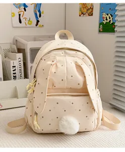 Vue de face d’un sac à dos crème à pois, avec oreilles de lapin, poche zippée et pompon doux