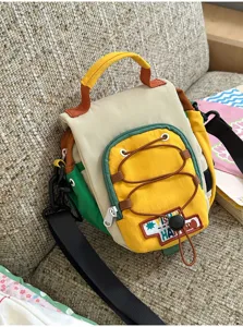 Sac coloré posé sur un canapé, avec poche jaune à cordon, poignée supérieure et bandoulière noire