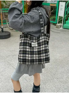 Outdoor view of a model carrying a black-and-white plaid tote, with its woven label visible