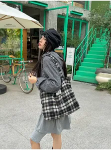 Street-style view of a model carrying a black-and-white checked tote beside green steps