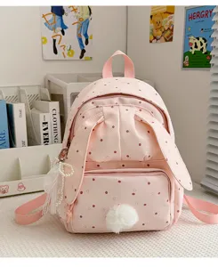 Vue de face d’un sac à dos rose pâle à pois, avec oreilles de lapin et pompon, présenté en intérieur