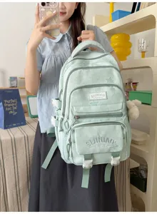 Une personne tient un sac menthe pâle à poches zippées, avec un petit pendentif en peluche.