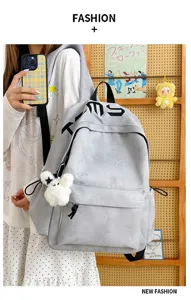 Vue portée d’un sac à dos gris à motif étoilé, poche zippée avant et pompon blanc en peluche