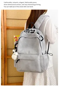 Sac à dos gris porté par un mannequin, avec gaufrage étoilé discret, lettres noires et pompon doux