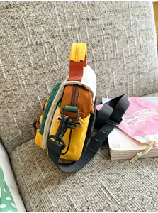 Vue latérale d’un petit sac à empiècements colorés, avec sangle noire et zip, posé sur un canapé