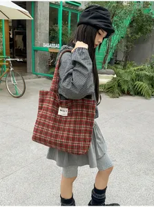 Outdoor street view of a model carrying a large red plaid tote bag over her shoulder