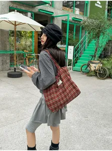 Outdoor street-style view of a red and green plaid fabric tote bag carried over one shoulder