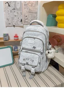 Détail d’un sac à dos gris clair avec poches zippées, sangles à boucle et ourson blanc en peluche