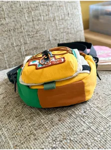 Vue rapprochée d’un sac jaune, vert et brun à empiècements, avec écusson brodé et cordon orange