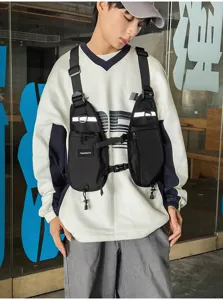 Model wearing a black chest bag with adjustable straps, buckles, front pockets and reflective trim