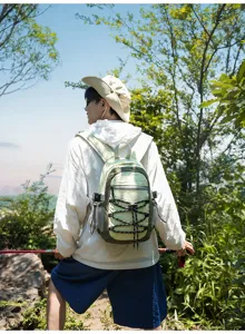 Outdooraufnahme einer Wanderin von hinten mit hellgrünem Rucksack und gekreuzten Bändern