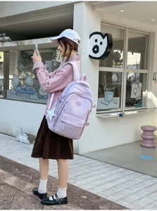 Vue de côté d’un sac à dos rose à texture pointillée et petit pendentif, porté en extérieur